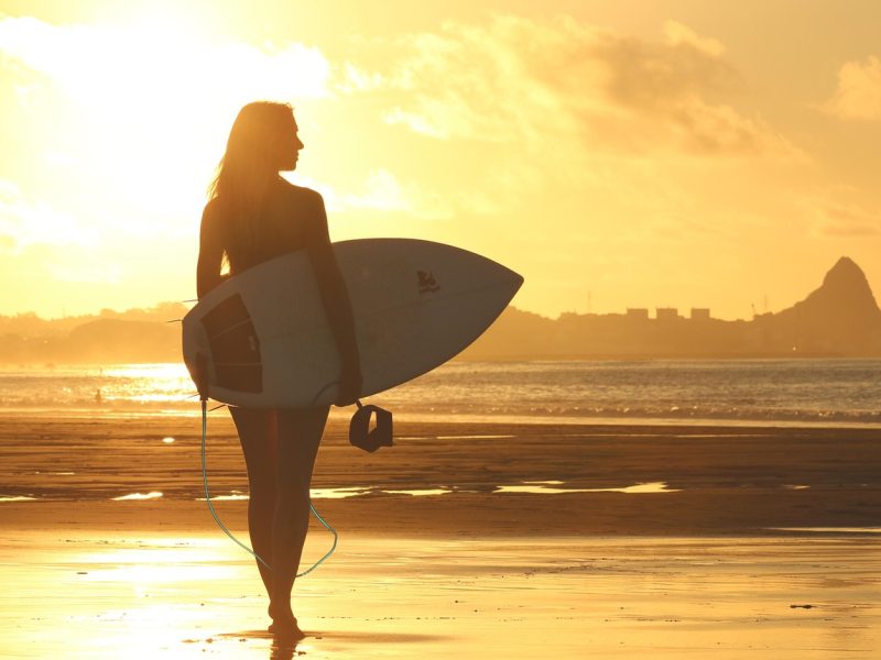 surfer walking towards ocean with surf board trinity esoterics