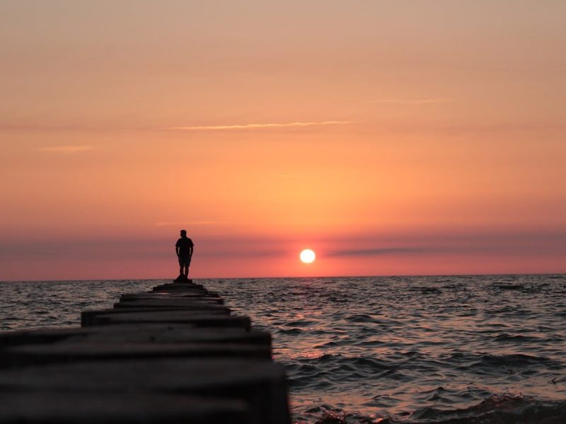person standing on top of rock pile overlooking choppy waters trinity esoterics