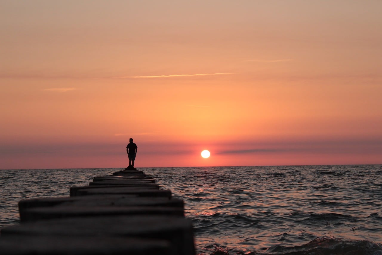person standing on top of rock pile overlooking choppy waters trinity esoterics